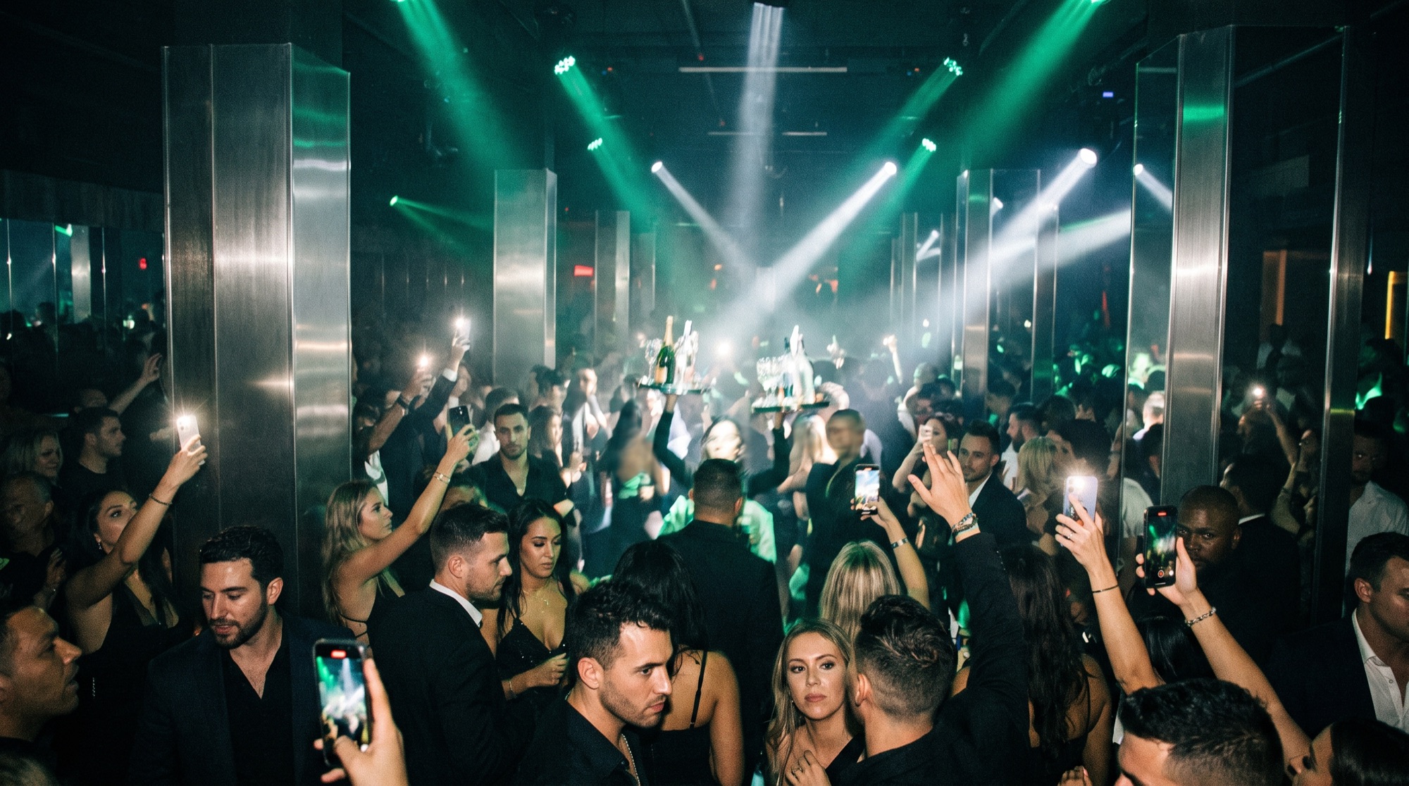 Packed nightclub under green beams and chrome pillars